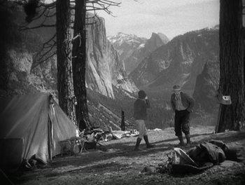 Two people walking near a tent in the mountains