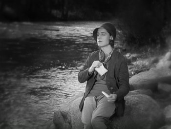 Movie still from “A Free Soul” (1931), directed by Clarence Brown – A person sitting on a rock near a body of water; Medium shot, High angle