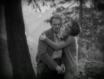 Movie still from “A Free Soul” (1931), directed by Clarence Brown – An older man and a young woman hugging in a forest; Medium shot, Low angle