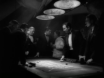 Movie still from “A Free Soul” (1931), directed by Clarence Brown – A group of people standing around a table with cards; Medium shot, High angle