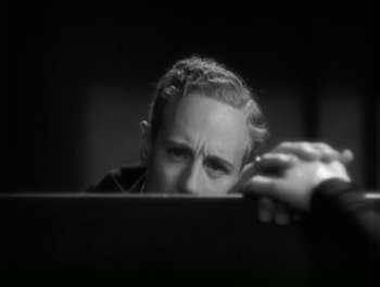 A black and white photo of a man leaning on a desk
