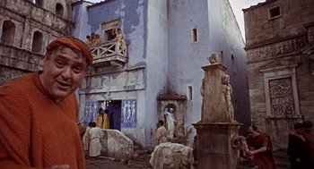 Movie still from “A Funny Thing Happened on the Way to the Forum” (1966), directed by Richard Lester – A group of people standing outside of a blue building; Wide shot, Low angle