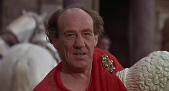 Movie still from “A Funny Thing Happened on the Way to the Forum” (1966), directed by Richard Lester – An older man wearing a red shirt and a gold medal; Close Up shot, Low angle