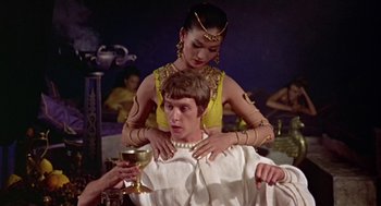Movie still from “A Funny Thing Happened on the Way to the Forum” (1966), directed by Richard Lester – A man sitting on the shoulders of a woman while holding a glass of wine; Medium shot, Low angle