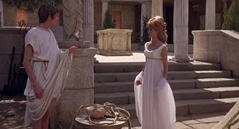 Movie still from “A Funny Thing Happened on the Way to the Forum” (1966), directed by Richard Lester – A woman in a white dress standing in front of a statue; Wide shot, Over the shoulder angle