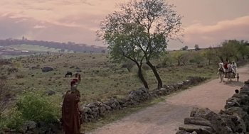 Movie still from “A Funny Thing Happened on the Way to the Forum” (1966), directed by Richard Lester – A man in a long brown coat standing next to a tree; Extreme Wide shot, High angle