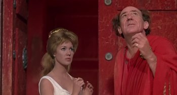 Movie still from “A Funny Thing Happened on the Way to the Forum” (1966), directed by Richard Lester – A man and a woman standing next to each other in front of a red wall; Medium shot, Low angle