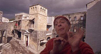 Movie still from “A Funny Thing Happened on the Way to the Forum” (1966), directed by Richard Lester – An old man in a red hat is standing in front of an old building; Medium shot, Overhead angle