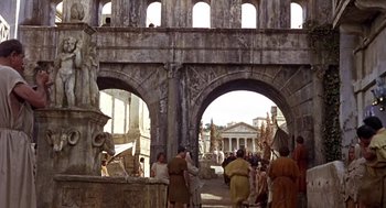 Movie still from “A Funny Thing Happened on the Way to the Forum” (1966), directed by Richard Lester – A group of people standing in front of an archway; Extreme Wide shot, Low angle
