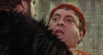 Movie still from “A Funny Thing Happened on the Way to the Forum” (1966), directed by Richard Lester – A man in a red hat is holding a black fur coat; Close Up shot, Over the shoulder angle
