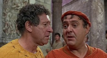 Movie still from “A Funny Thing Happened on the Way to the Forum” (1966), directed by Richard Lester – Two men are talking to each other while wearing orange; Close Up shot, Over the shoulder angle
