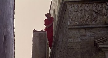 Movie still from “A Funny Thing Happened on the Way to the Forum” (1966), directed by Richard Lester – A man in a red suit climbing a wall; Wide shot, Low angle