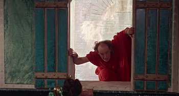 Movie still from “A Funny Thing Happened on the Way to the Forum” (1966), directed by Richard Lester – A man in a red shirt leaning against a window sill; Medium shot, High angle