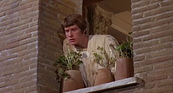 Movie still from “A Funny Thing Happened on the Way to the Forum” (1966), directed by Richard Lester – A man standing next to potted plants on a window ledge; Medium shot, Low angle