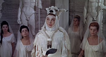 Movie still from “A Funny Thing Happened on the Way to the Forum” (1966), directed by Richard Lester – A woman dressed in white with a goat head on her head; Medium shot, Low angle