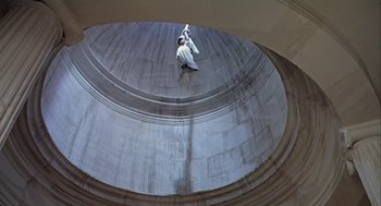 Movie still from “A Funny Thing Happened on the Way to the Forum” (1966), directed by Richard Lester – A man in a white shirt is standing in the middle of a building; Extreme Wide shot, Overhead angle