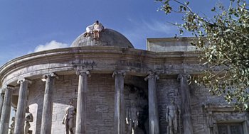 Movie still from “A Funny Thing Happened on the Way to the Forum” (1966), directed by Richard Lester – A man sitting on top of a dome on top of a building; Extreme Wide shot, Low angle