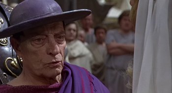 Movie still from “A Funny Thing Happened on the Way to the Forum” (1966), directed by Richard Lester – An old man wearing a purple hat and a purple robe; Close Up shot, Over the shoulder angle