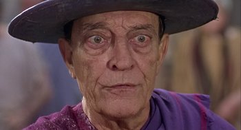 Movie still from “A Funny Thing Happened on the Way to the Forum” (1966), directed by Richard Lester – An old man wearing a purple shirt and a black hat; Close Up shot, Low angle