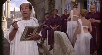 Movie still from “A Funny Thing Happened on the Way to the Forum” (1966), directed by Richard Lester – A man in a toga costume singing in front of a group of people; Medium shot, Over the shoulder angle