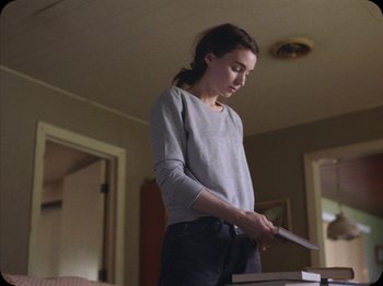 Movie still from “A Ghost Story” (2017), directed by David Lowery – A woman standing in front of a table cutting paper; Medium shot, Over the shoulder angle