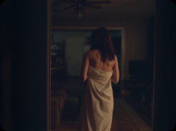 Movie still from “A Ghost Story” (2017), directed by David Lowery – A woman wrapped in a towel in a living room; Medium shot, Over the shoulder angle