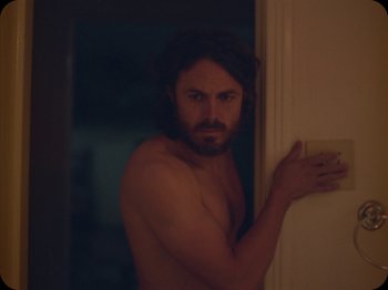 Movie still from “A Ghost Story” (2017), directed by David Lowery – A shirtless man leaning against a wall in the dark; Medium shot, Over the shoulder angle
