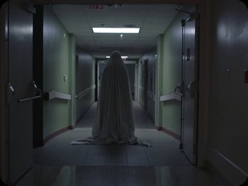 Movie still from “A Ghost Story” (2017), directed by David Lowery – A person that is dressed as a ghost in a hallway; Wide shot, Low angle