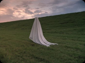 Movie still from “A Ghost Story” (2017), directed by David Lowery – A white sheet sitting on top of a grass covered field; Extreme Wide shot, Low angle