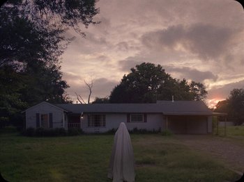 Movie still from “A Ghost Story” (2017), directed by David Lowery – An image of a person that is standing in the grass; Extreme Wide shot, Low angle