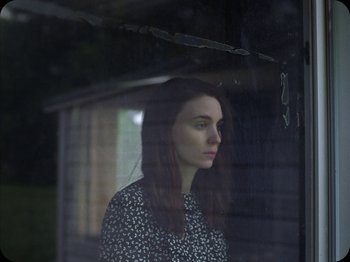 Movie still from “A Ghost Story” (2017), directed by David Lowery – A woman standing in front of a window looking sad; Close Up shot, Low angle