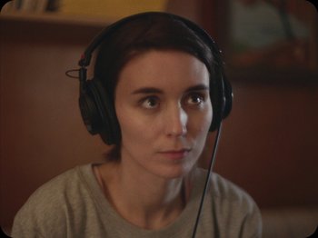 Movie still from “A Ghost Story” (2017), directed by David Lowery – A woman wearing headphones and sitting in front of a window; Close Up shot, Over the shoulder angle