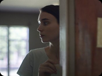 Movie still from “A Ghost Story” (2017), directed by David Lowery – A woman standing in front of a door looking out a window; Close Up shot, Over the shoulder angle