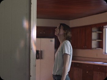 Movie still from “A Ghost Story” (2017), directed by David Lowery – A woman standing in a kitchen with her eyes wide open; Medium shot, Over the shoulder angle