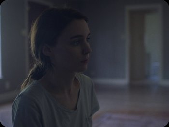 Movie still from “A Ghost Story” (2017), directed by David Lowery – A woman in a white shirt is in a dark room; Close Up shot, Over the shoulder angle