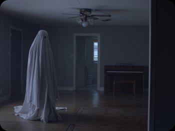 Movie still from “A Ghost Story” (2017), directed by David Lowery – A person that is standing in a room; Wide shot, Over the shoulder angle