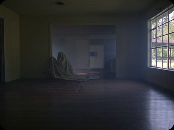 Movie still from “A Ghost Story” (2017), directed by David Lowery – An image of a person hiding in a living room; Extreme Wide shot, Low angle