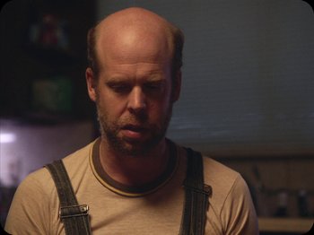 Movie still from “A Ghost Story” (2017), directed by David Lowery – A man with a bald head is standing in a room; Close Up shot, Over the shoulder angle