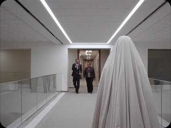 Movie still from “A Ghost Story” (2017), directed by David Lowery – Two men in suits and one is wearing a white sheet; Wide shot, Over the shoulder angle