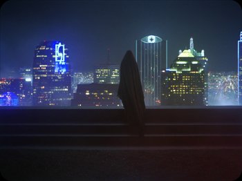 Movie still from “A Ghost Story” (2017), directed by David Lowery – A person standing on a ledge in front of a city skyline; Extreme Wide shot, Low angle