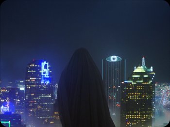 Movie still from “A Ghost Story” (2017), directed by David Lowery – A person standing in front of a city at night; Extreme Wide shot, Low angle