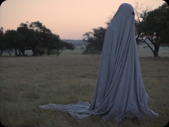 Movie still from “A Ghost Story” (2017), directed by David Lowery – A person in a sheet standing in a field; Medium shot, Over the shoulder angle