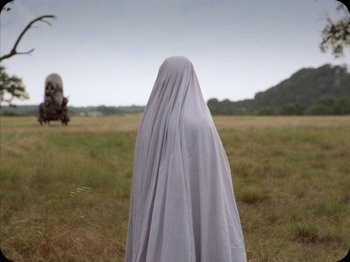 Movie still from “A Ghost Story” (2017), directed by David Lowery – A person with a white sheet on a field; Medium shot, Low angle