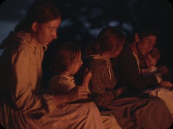 Movie still from “A Ghost Story” (2017), directed by David Lowery – A group of people sitting on a blanket at night; Medium shot, Over the shoulder angle