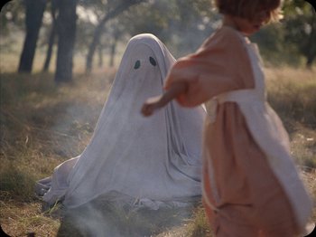 Movie still from “A Ghost Story” (2017), directed by David Lowery – A little girl is running behind a ghost in a field; Medium shot, High angle