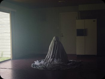 Movie still from “A Ghost Story” (2017), directed by David Lowery – A person is covered in a blanket in a room; Wide shot, High angle