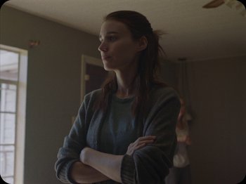 Movie still from “A Ghost Story” (2017), directed by David Lowery – A woman standing with her arms crossed in a room; Medium shot, Over the shoulder angle