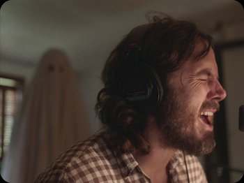 Movie still from “A Ghost Story” (2017), directed by David Lowery – A man with a beard wearing headphones and a shirt; Close Up shot, Low angle