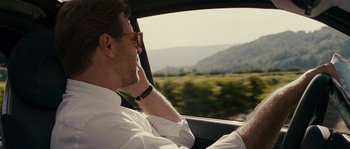 Movie still from “A Good Year” (2006), directed by Ridley Scott – A man driving a car while talking on a cell phone; Close Up shot, Over the shoulder angle