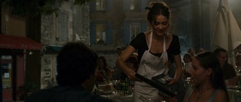 Movie still from “A Good Year” (2006), directed by Ridley Scott – A woman in an apron is serving a person; Medium shot, Over the shoulder angle